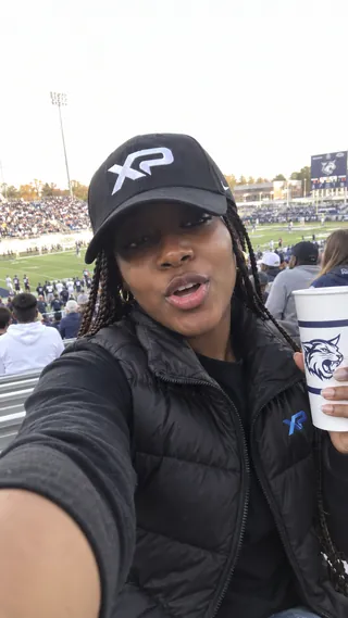Ambassador content mockup of a student wearing an XtraPoint cap and shirt in the stadium stands.